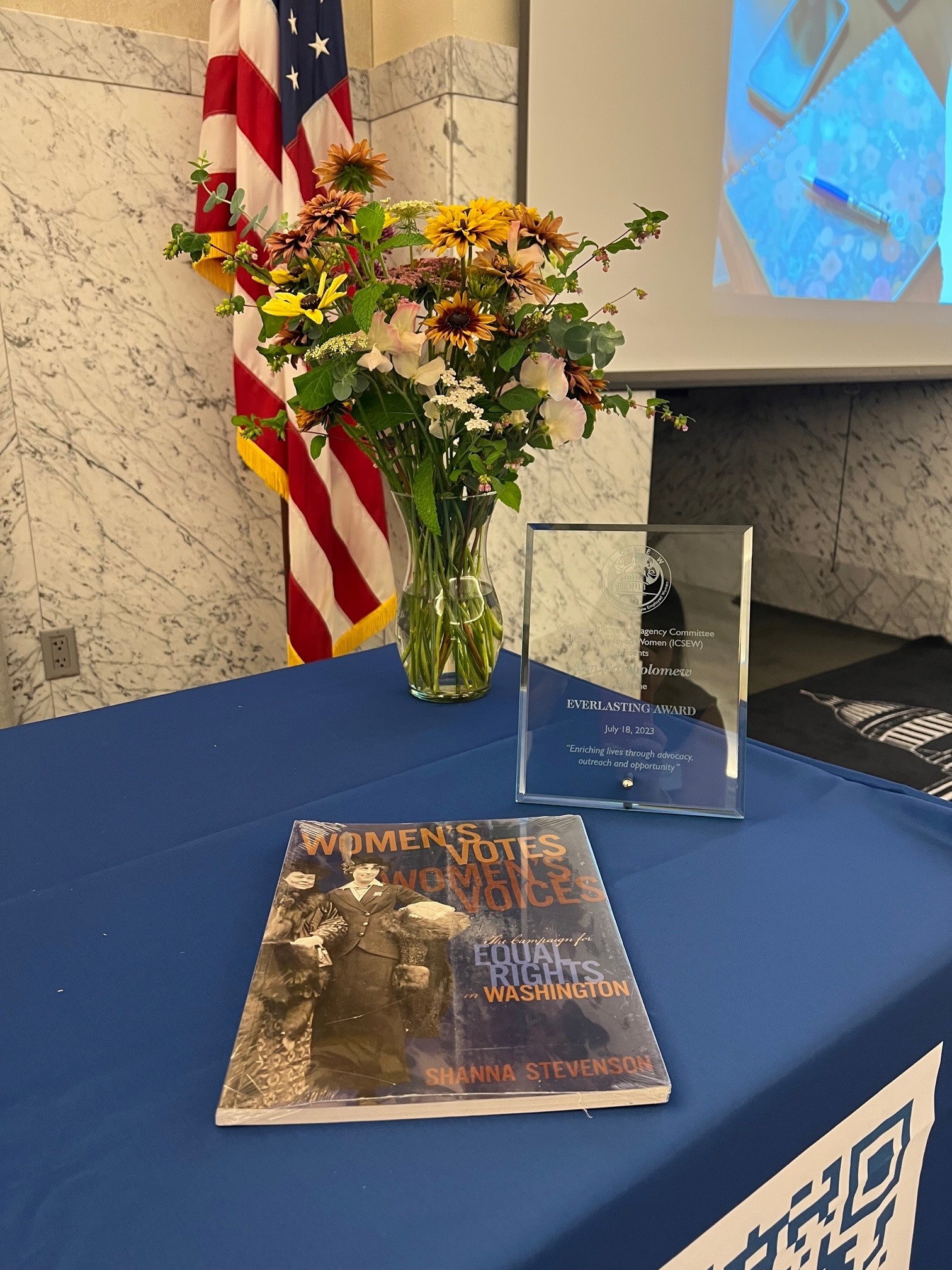 image of ICSEW award on table next to flower vase and book on women's history